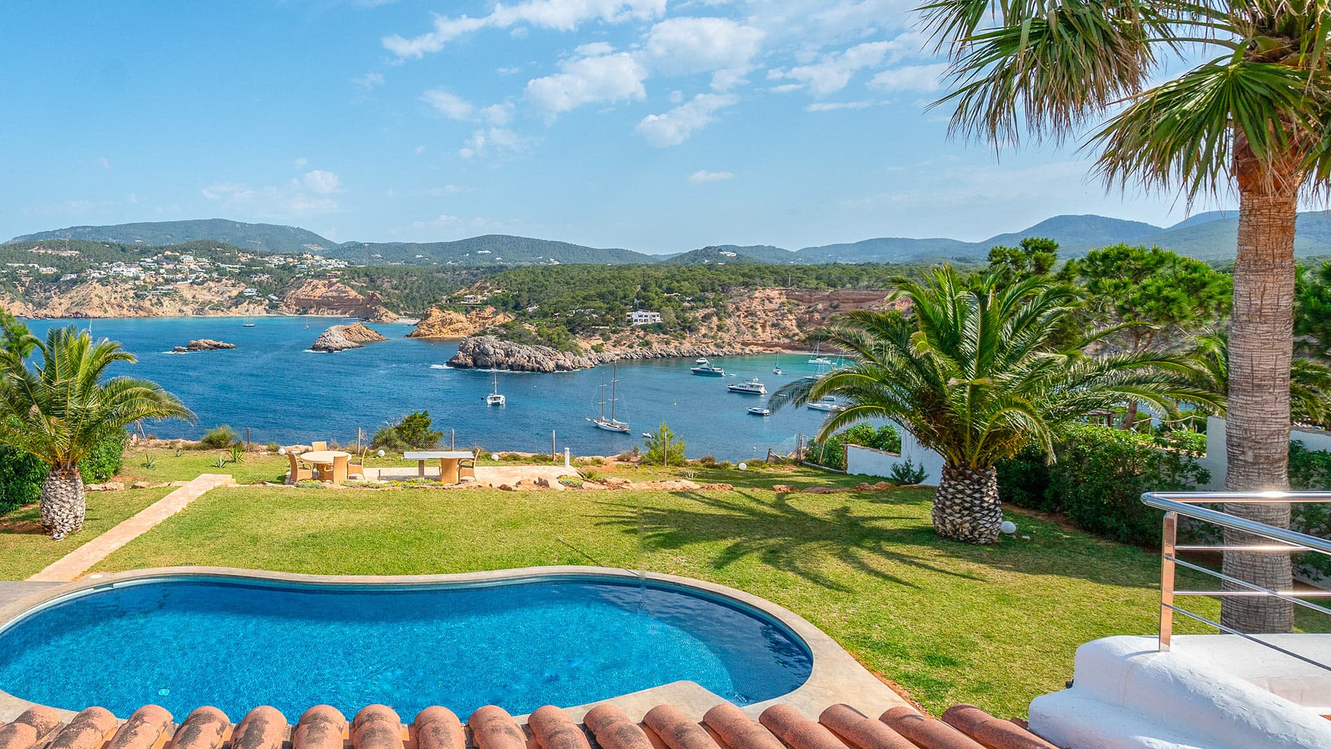 Lawn and swimming pool with the bay beyond at Casa Porroig, Es Cubells, Ibiza