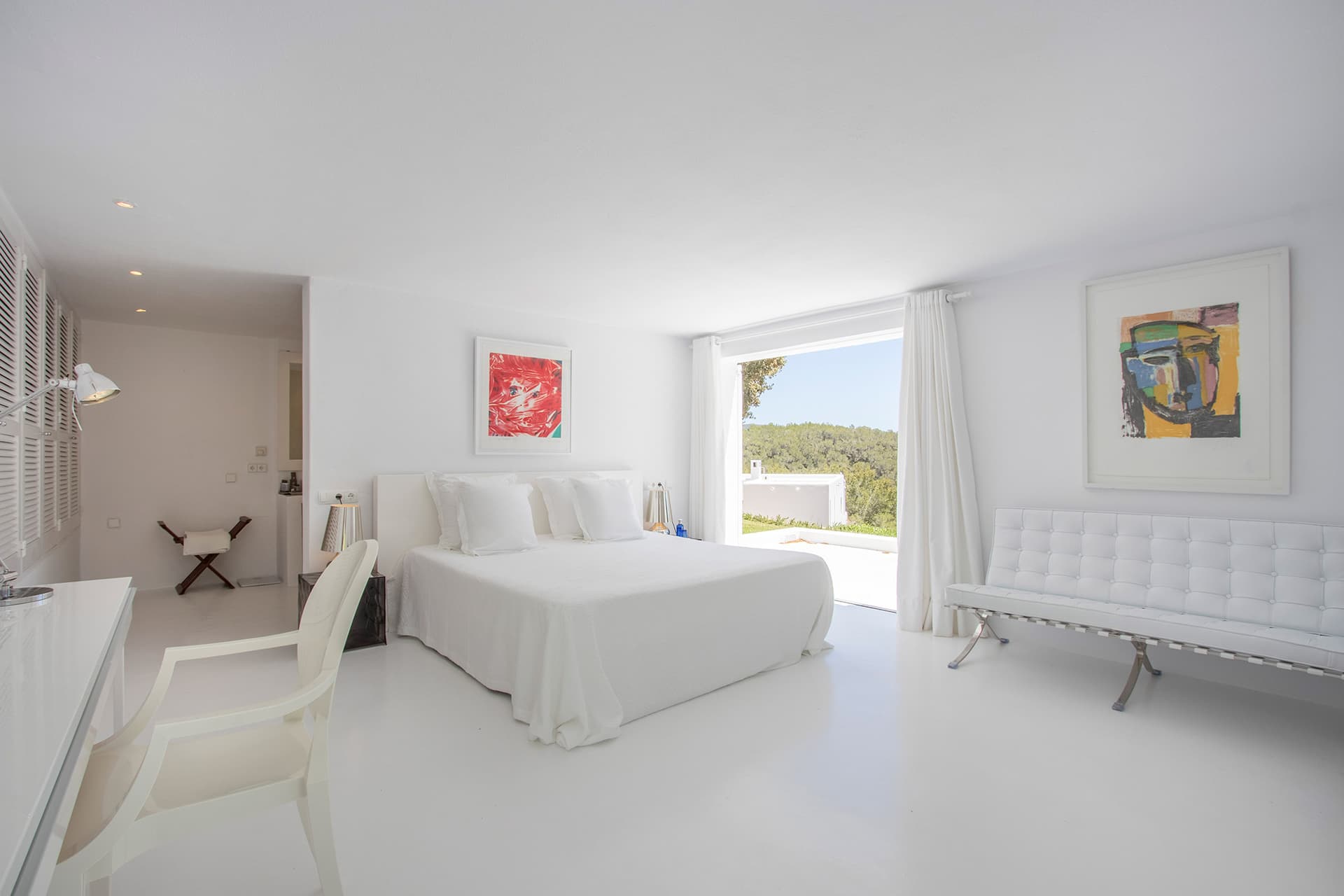Minimal white bedroom with artwork and a window to the garden at Villa Predo, Es Cubells, Ibiza