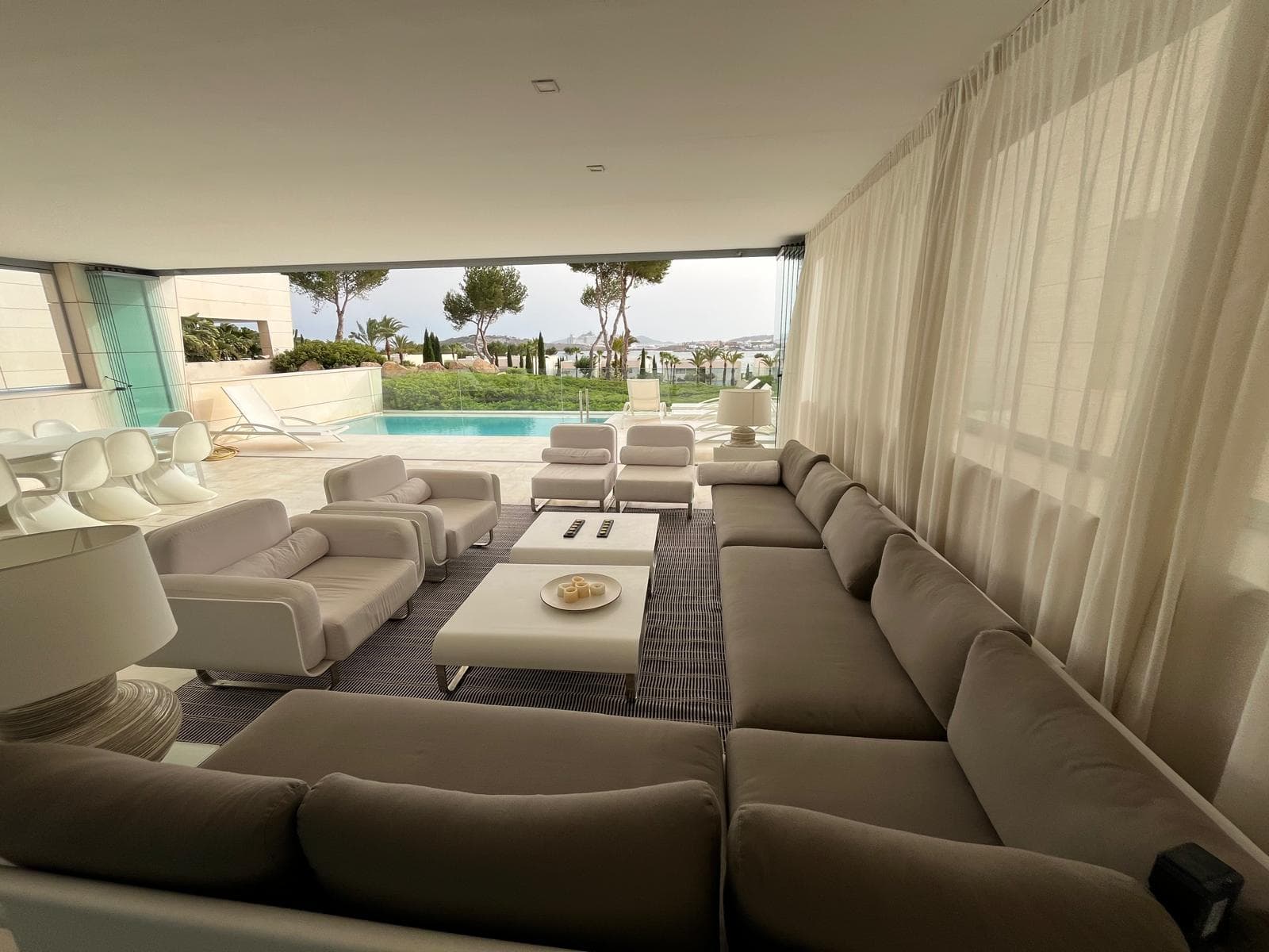 Living room with white sofas and linen curtains opening towards the pool, private urbanisation, Ibiza