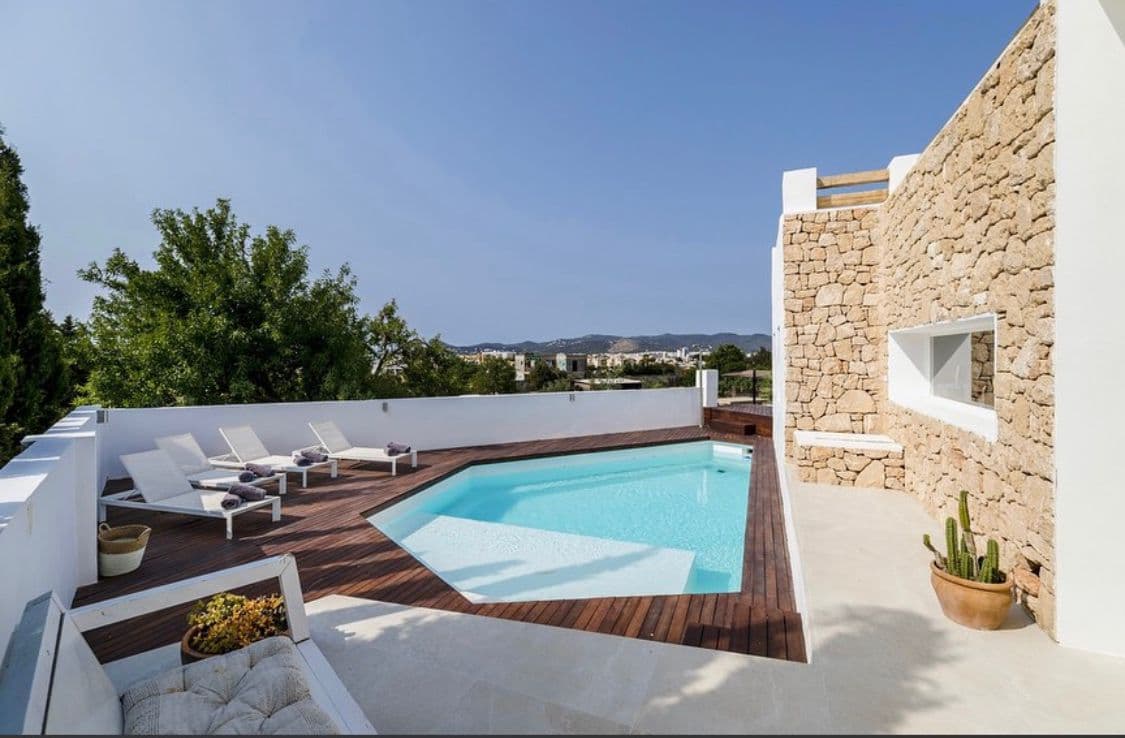 Rooftop pool terrace with wooden deck, sun loungers and a natural stone wall, overlooking distant hills at this Sant Josep villa.