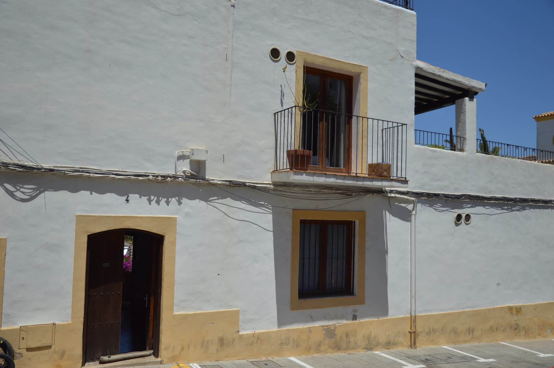 Exterior wall of Casa Mor in Dalt de la Vila with a wooden door, shuttered windows and a small wrought iron balcony holding potted plants.
