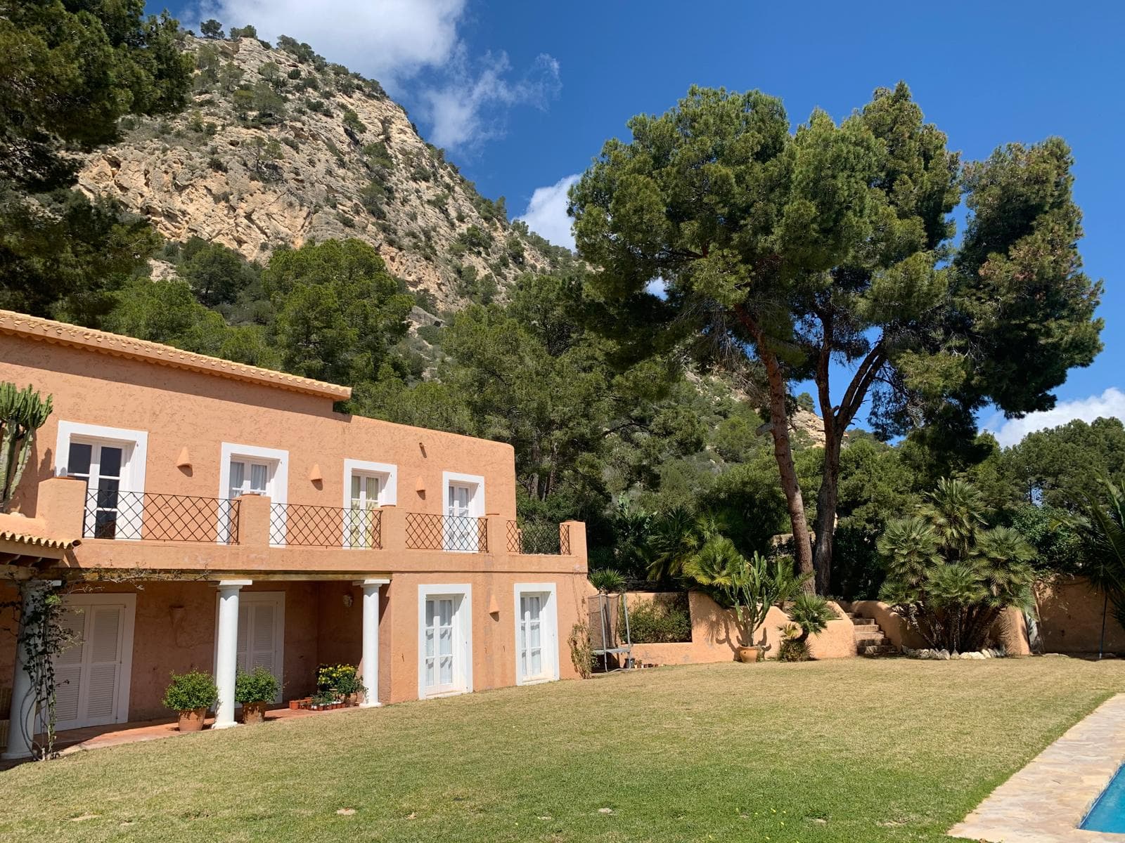 Terracotta rendered house with lawns and mature palms at Casa Hermosa, Es Cubells, Ibiza