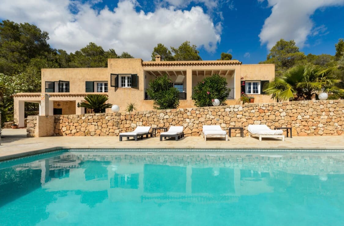 Turquoise pool and sun loungers below the stone facade of a family villa, Sant Josep, Ibiza