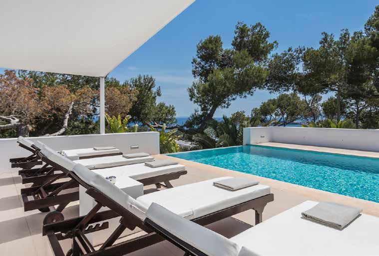 Swimming pool with sun loungers set between the pines above the sea at Villa Blanca, Cap Martinet, Ibiza