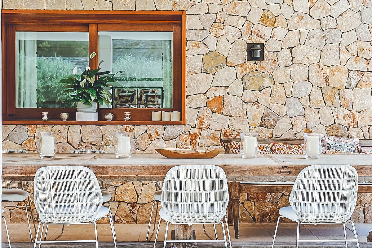 Alfresco dining table in reclaimed wood with woven rattan chairs beside a traditional Ibicenco dry stone wall