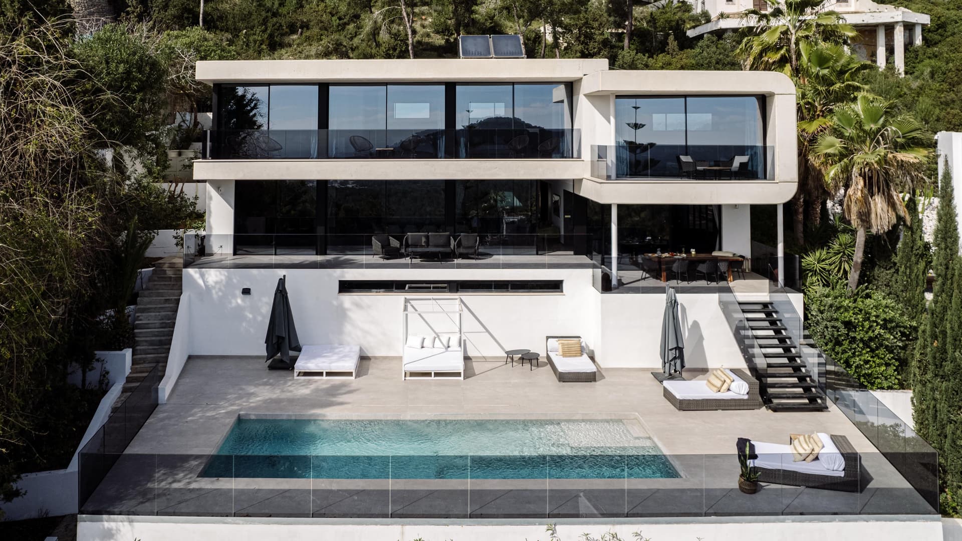 Swimming pool below the dark framed glazing and palms at Villa Casanova, Jesus, Ibiza