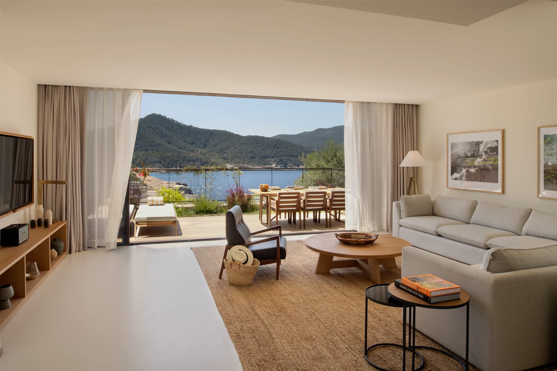 Living room in warm neutrals opening onto the terrace with the bay beyond, a four bedroom residence in Portinatx, Ibiza