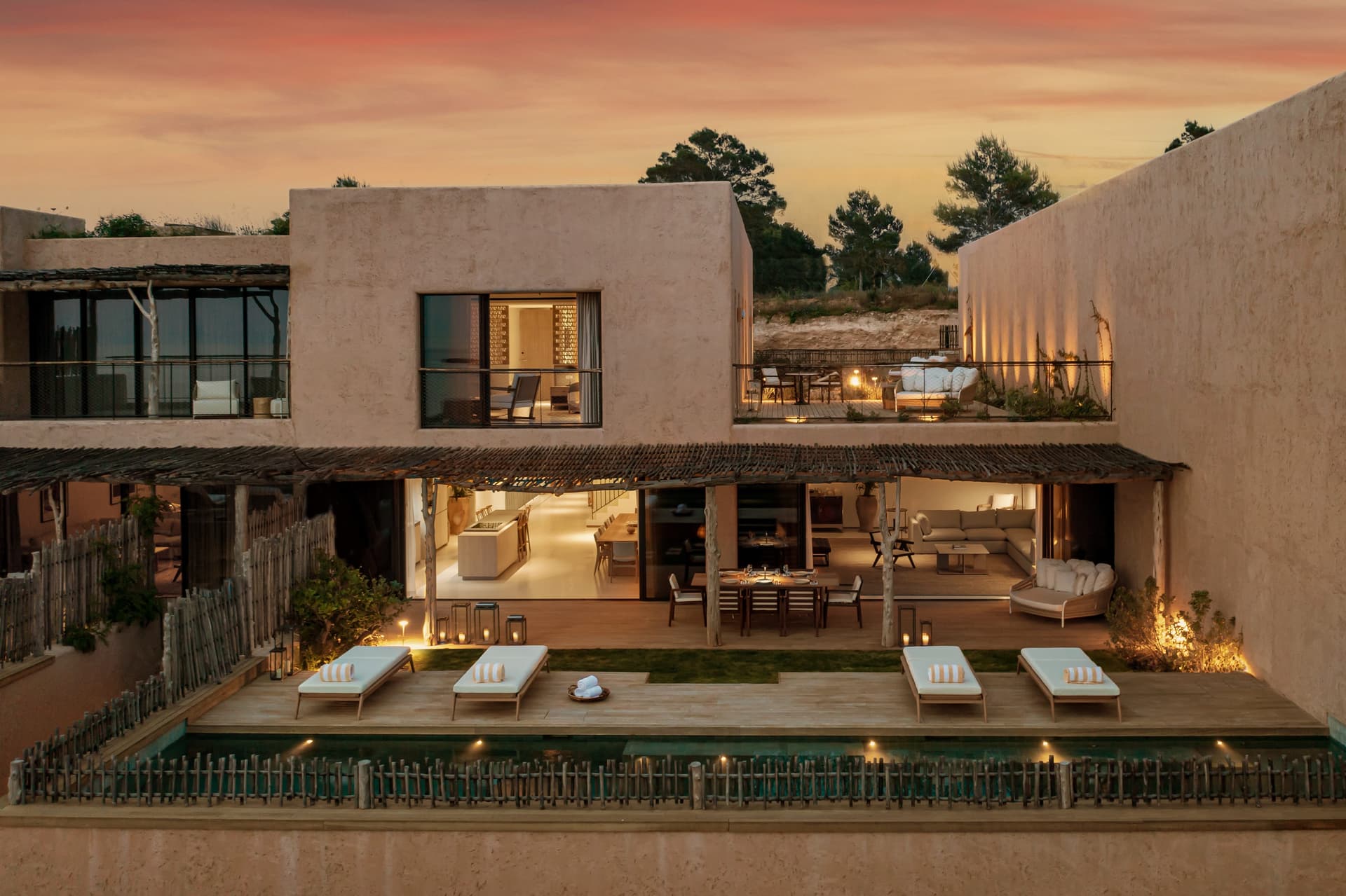 Sandstone villa lit at dusk with sun loungers beside the pool, Portinatx, Ibiza