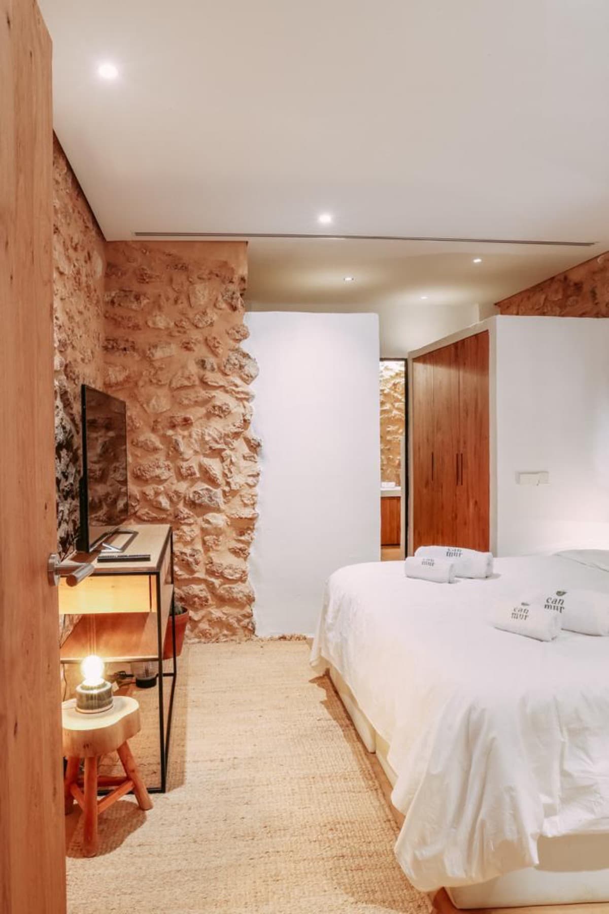 Bedroom with a dry stone feature wall and white linen at Can Lucy Jondal, Cala Jondal, Ibiza