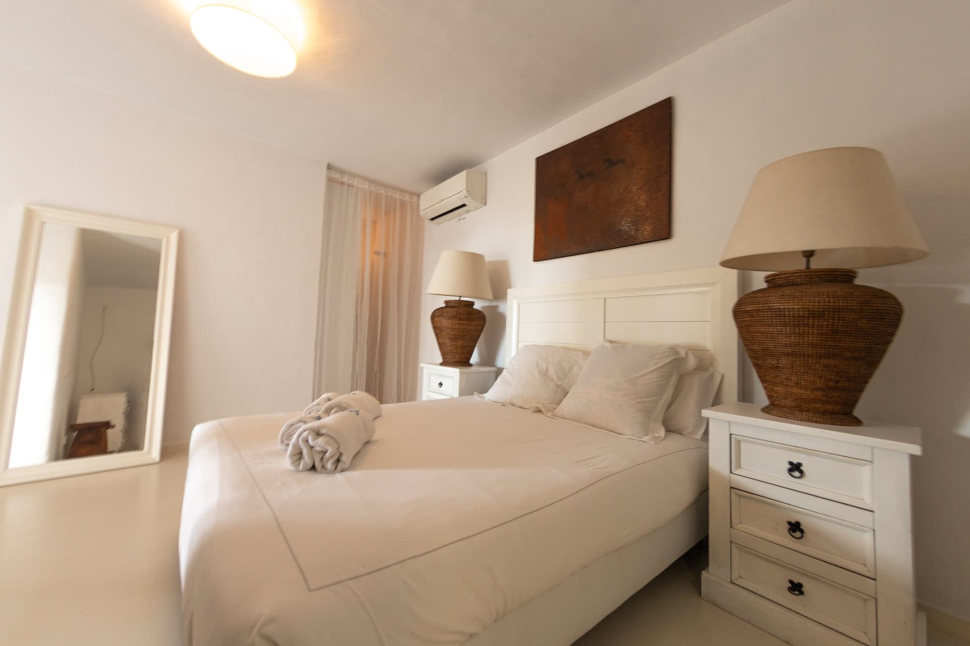 Simple white bedroom with a dark timber chest at Villa Margo, Sant Josep, Ibiza