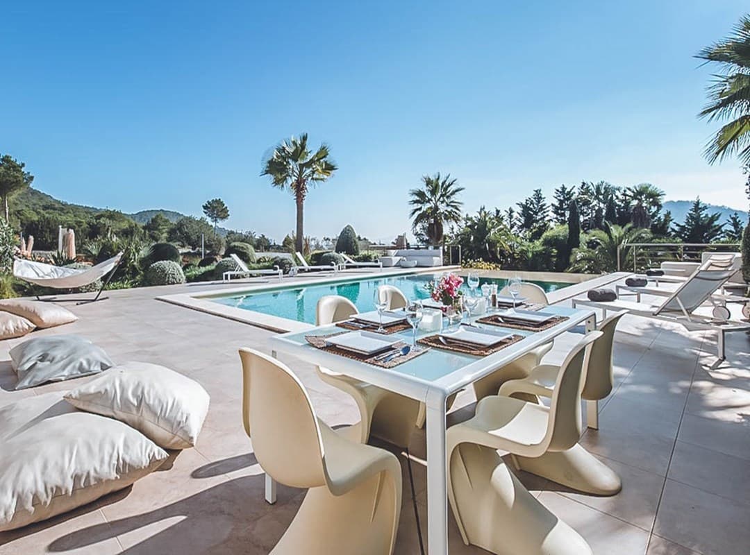 Outdoor dining with white chairs looking over the pool to the hills at Villa Nia, Cala Jondal, Ibiza