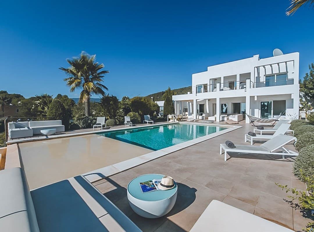 Swimming pool with a palm and sun loungers below the white terraces at Villa Nia, Cala Jondal, Ibiza