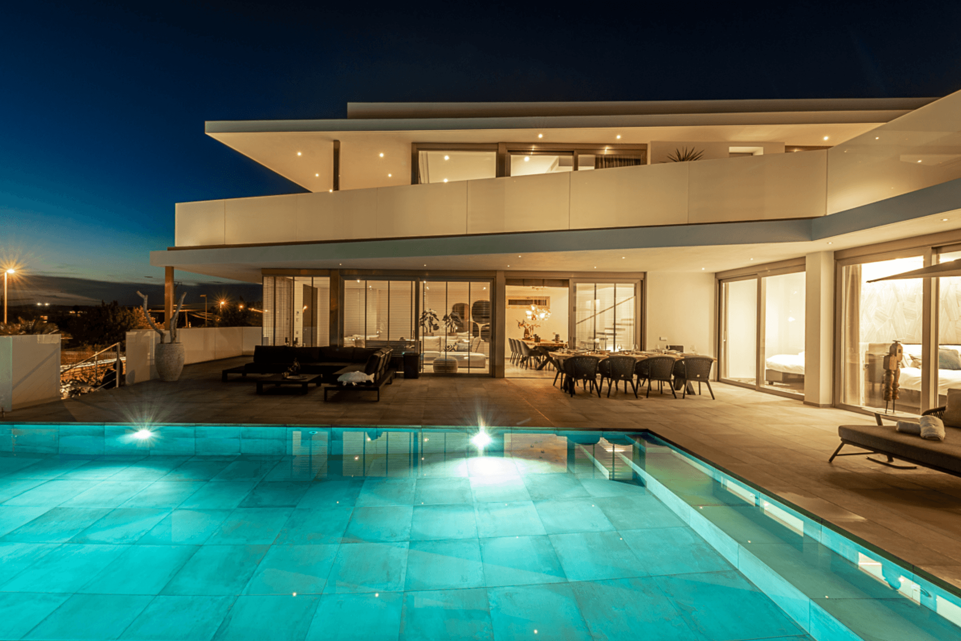 Newly built chalet lit at dusk with its pool and glazed living spaces, with views to Dalt Vila, Ibiza