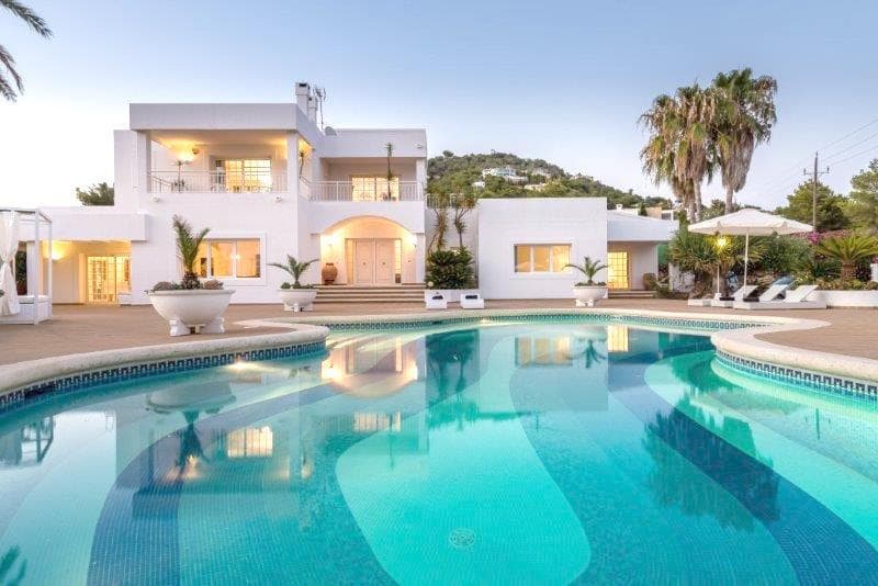 Large curved swimming pool lit at dusk below the white facade, Cap Martinet, Ibiza